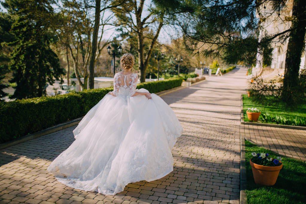 Una bella sposa con i capelli biondi che corre agitando il vestito il giorno del matrimonio. vista posteriore
 - Foto, immagini