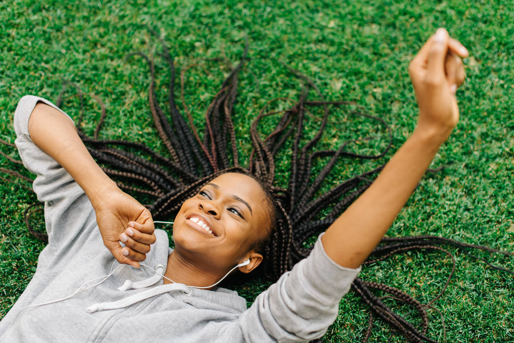 Boven staand van de vreugdevolle Afro-Amerikaanse tiener opleggen aan het gras, terwijl het luisteren naar muziek en bewegen de handen. - Foto, afbeelding