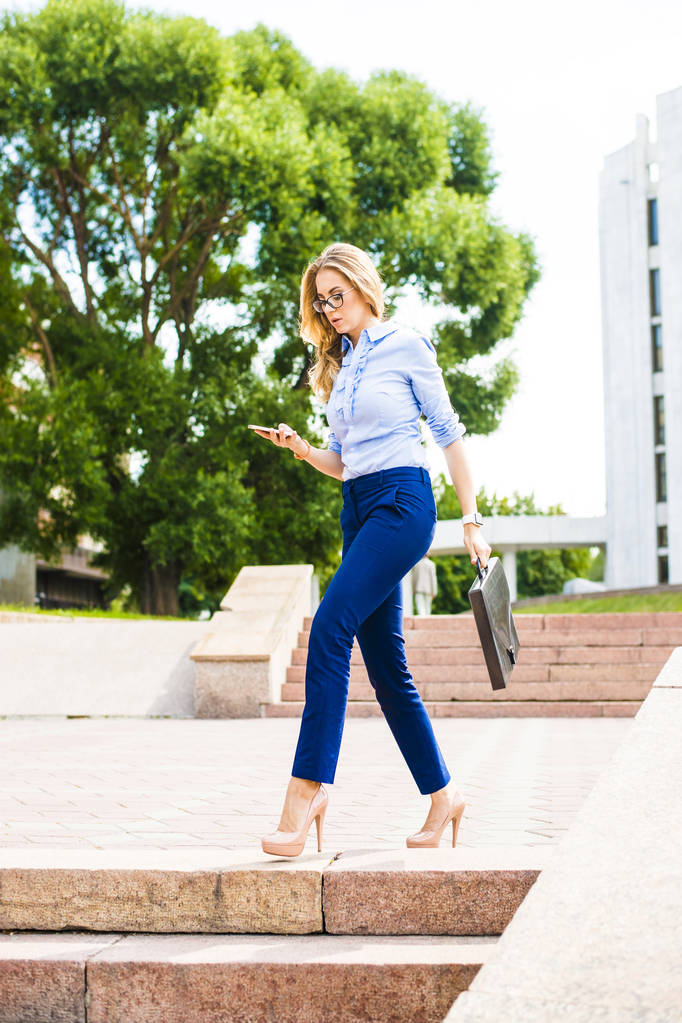 busy blond businesswoman walking with mobile phone on street - Photo, Image