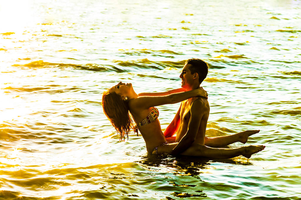 Két fiatal felnőtt szerelmeseinek állandó víz naplementekor  - Fotó, kép