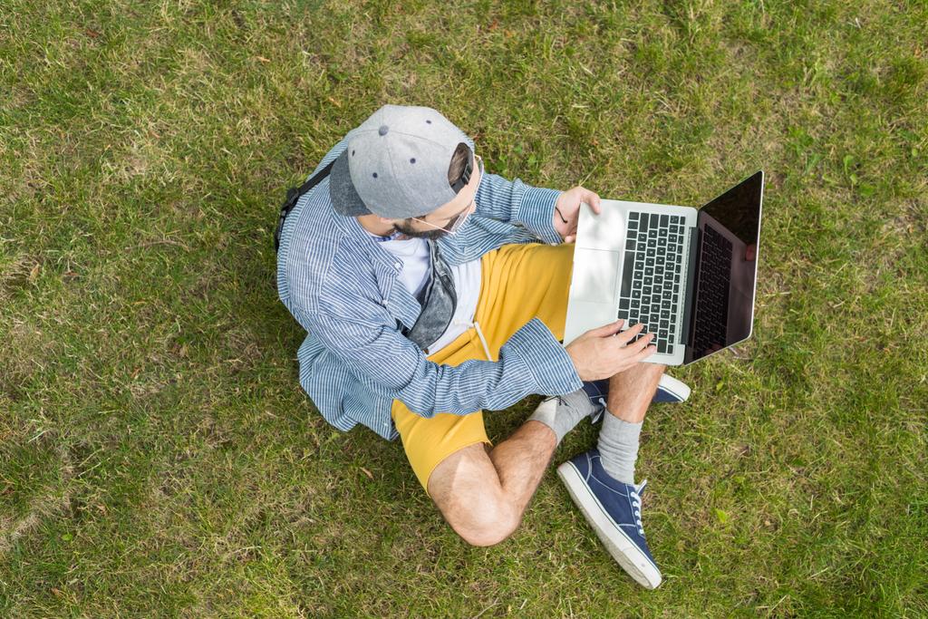 Mies kannettava tietokone istuu nurmikolla
 - Valokuva, kuva