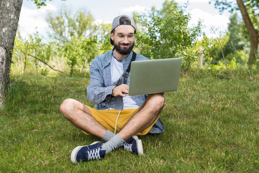 Mies kannettava tietokone istuu nurmikolla
 - Valokuva, kuva