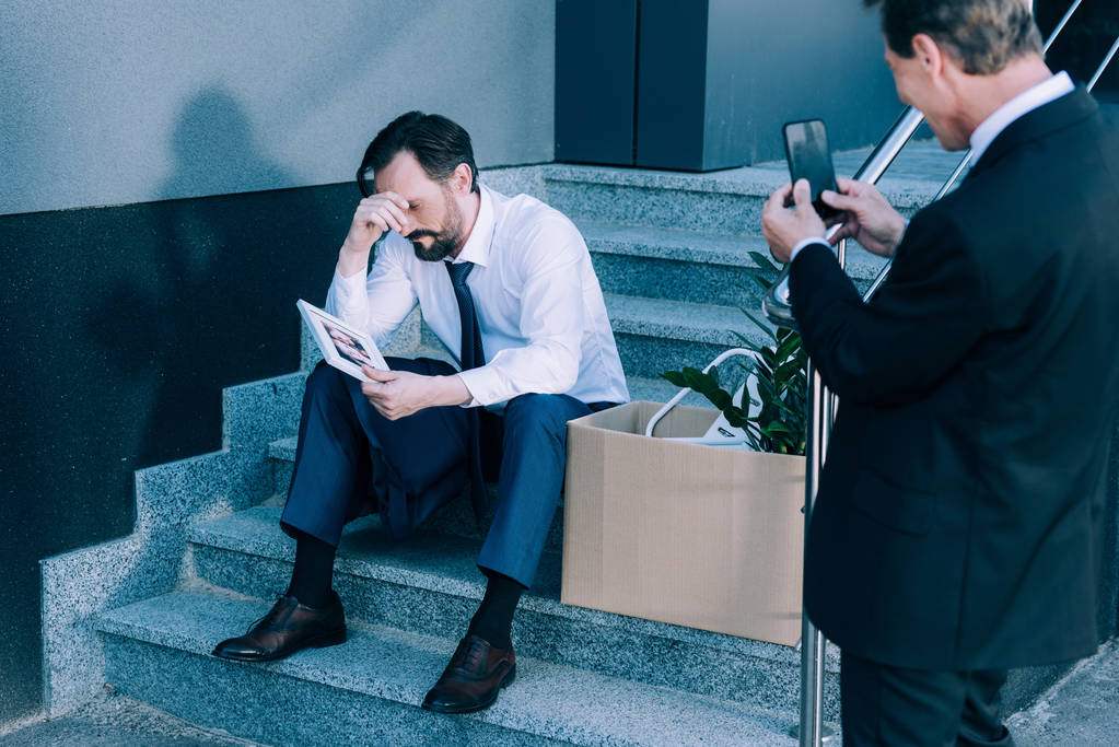бизнесмен со смартфоном фотографирует уволенного коллегу
 - Фото, изображение