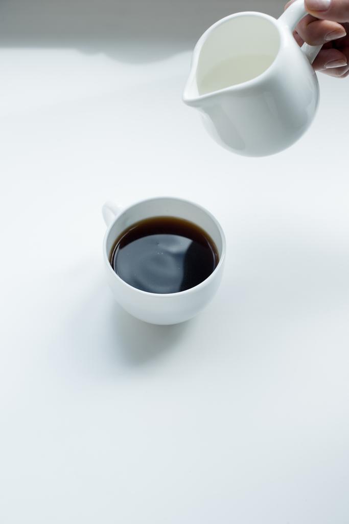 kaatamalla maitoa kuppiin mustaa kahvia
  - Valokuva, kuva