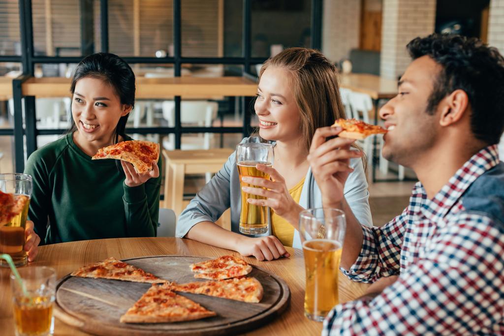 vrienden eten pizza met bier in café - Foto, afbeelding