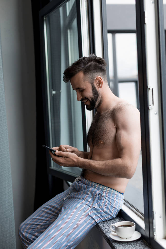 paidaton mies käyttää älypuhelinta ikkunalaudalla
 - Valokuva, kuva