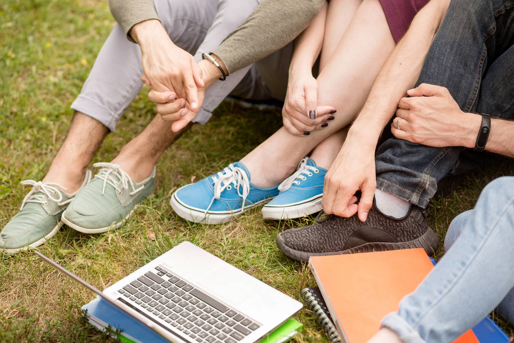 Close-up vista sobre pernas e mãos de estudantes sentados na grama
. - Foto, Imagem