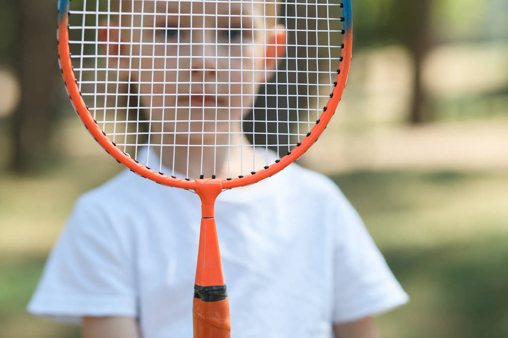 Retrato de pequeno rapaz atrás de uma raquete de badminton em uma floresta de pinheiro, resto ativo em uma natureza
 - Foto, Imagem