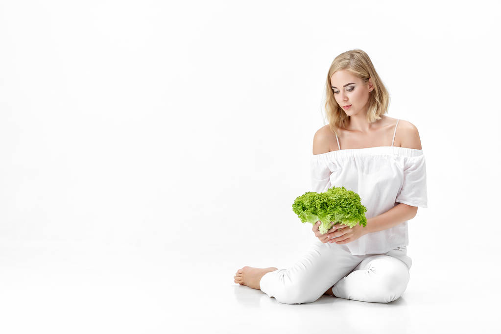 Mooie blonde vrouw in witte blouse met frisse groene salade op witte achtergrond. Gezondheid en dieet - Foto, afbeelding