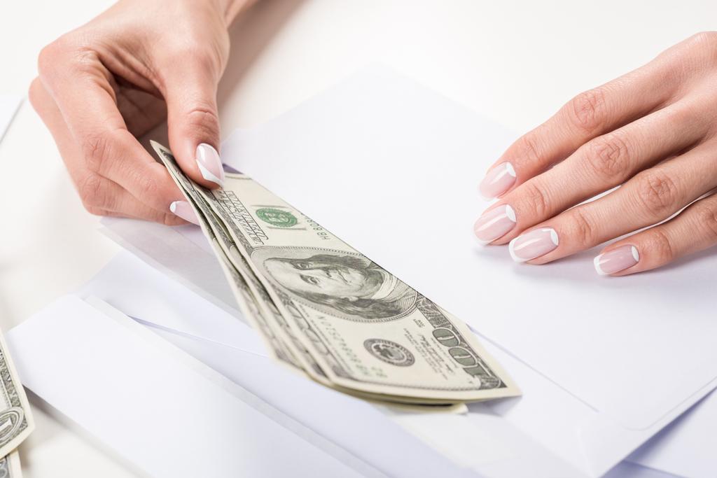 vrouwelijke handen met dollar biljetten in envelop   - Foto, afbeelding