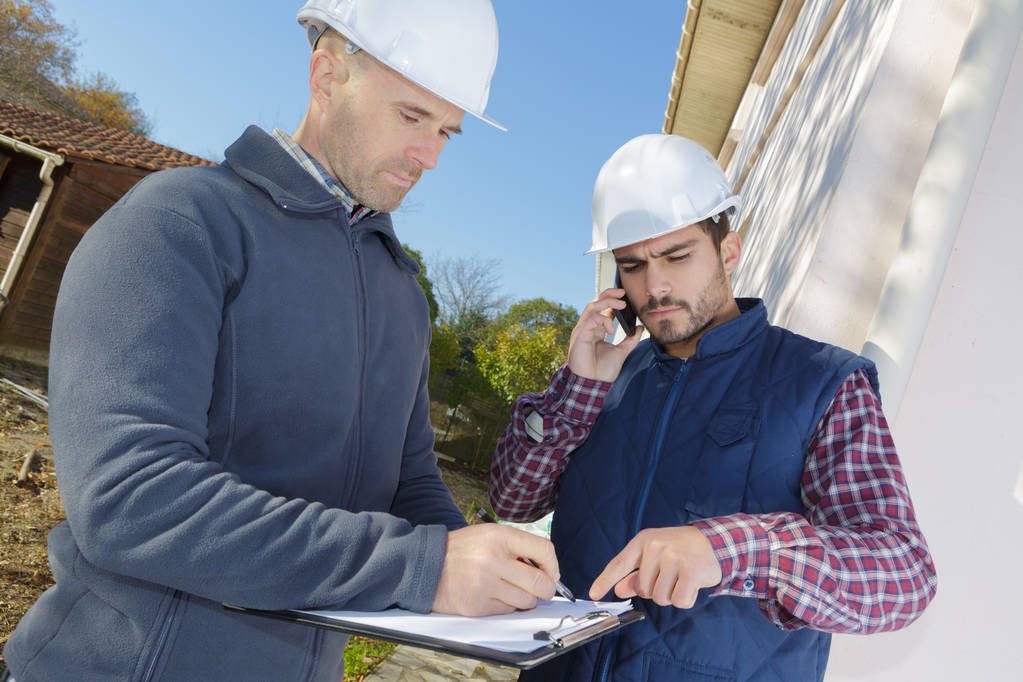 інженер-будівельник розмовляє по телефону під час перевірки прогресу будівлі
 - Фото, зображення