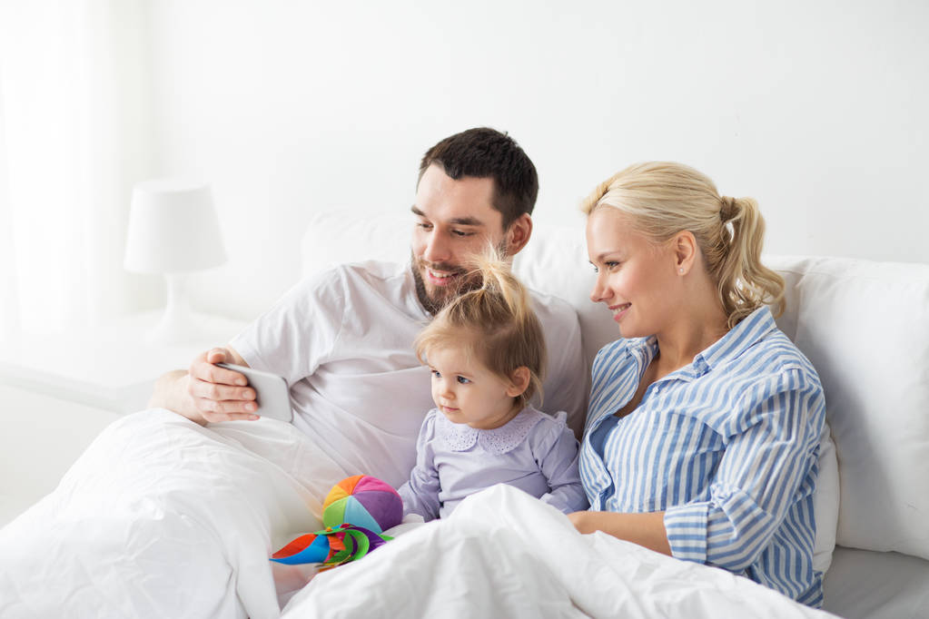 ευτυχισμένη οικογένεια με smartphone στο κρεβάτι στο σπίτι - Φωτογραφία, εικόνα