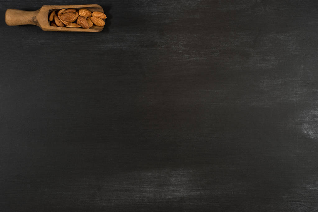 Amandelen in een houten lepel in een zwarte schoolbord.  - Foto, afbeelding