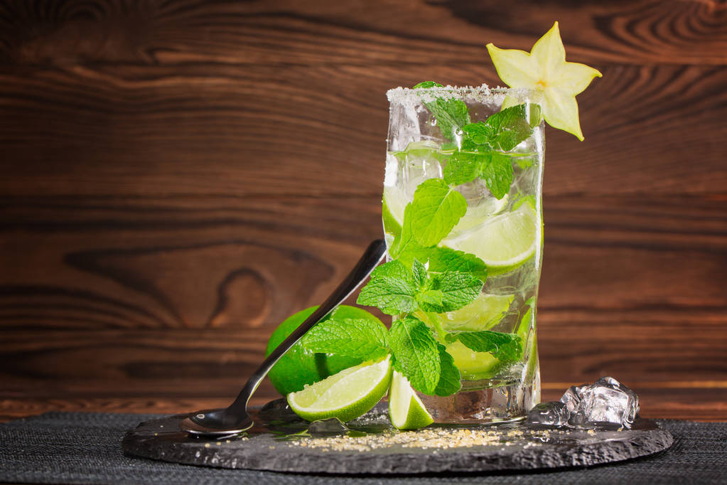 Refreshing cocktail mojito with rum, fresh lime, mint, crushed ice and carambola on a dark wooden background. A glass full of alcohol mojito. Copy space. - Photo, Image