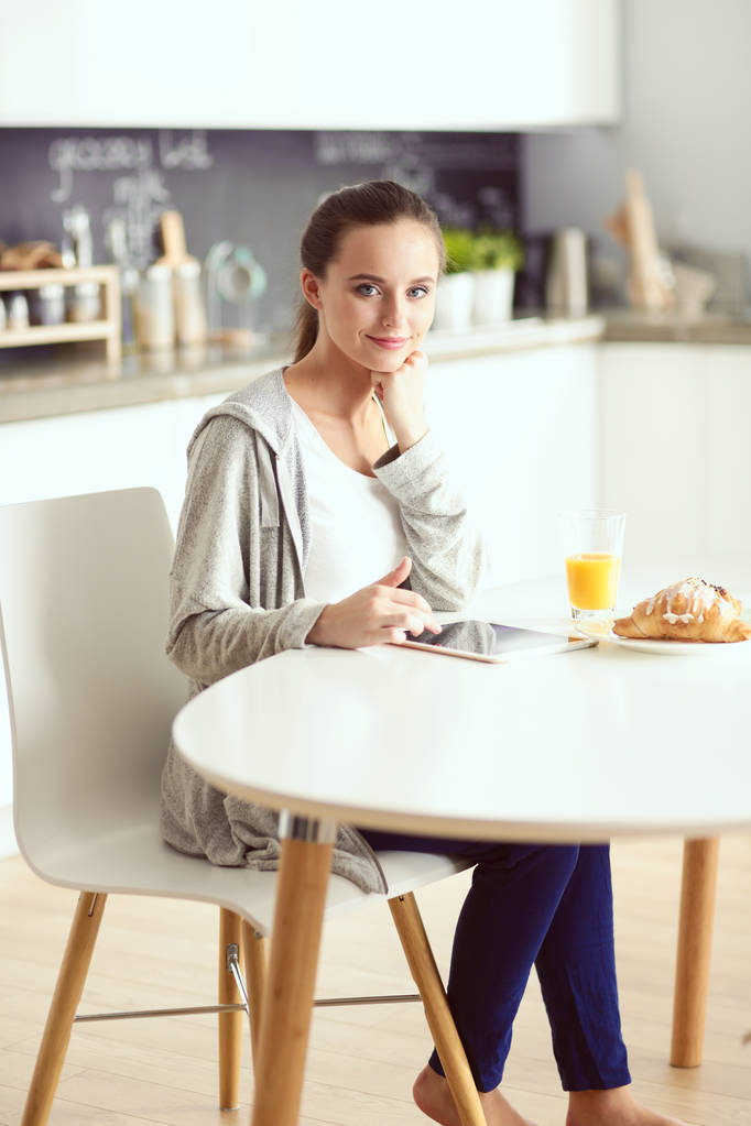 Jonge vrouw met sinaasappelsap en tablet in keuken. - Foto, afbeelding