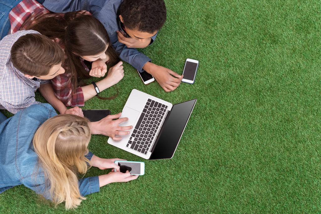 adolescentes multiétnicos con ordenador portátil en el césped verde
 - Foto, Imagen