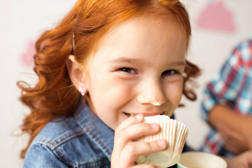 かわいい赤毛の女の子甘いカップケーキを食べるとカメラ目線 ロイヤリティフリー写真 画像素材