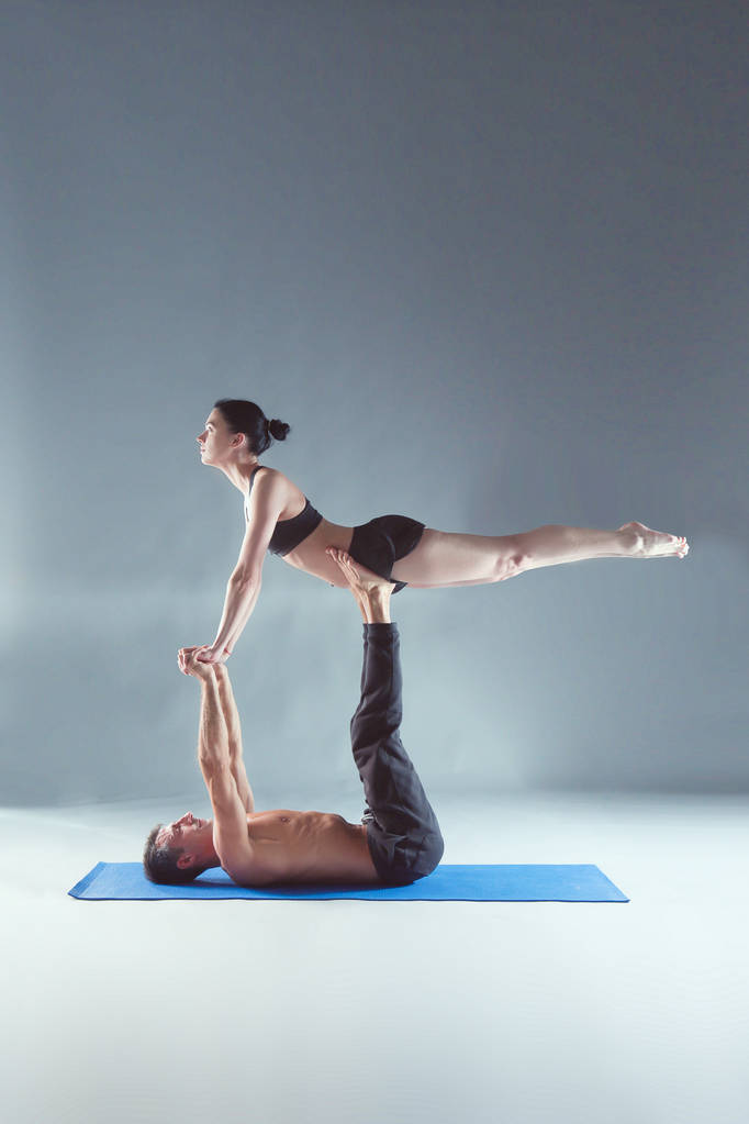 Νεαρό ζευγάρι εξάσκηση acro yoga σε χαλί στο στούντιο μαζί. Acroyoga. Γιόγκα ζευγάρι. Εταίρους γιόγκα. - Φωτογραφία, εικόνα