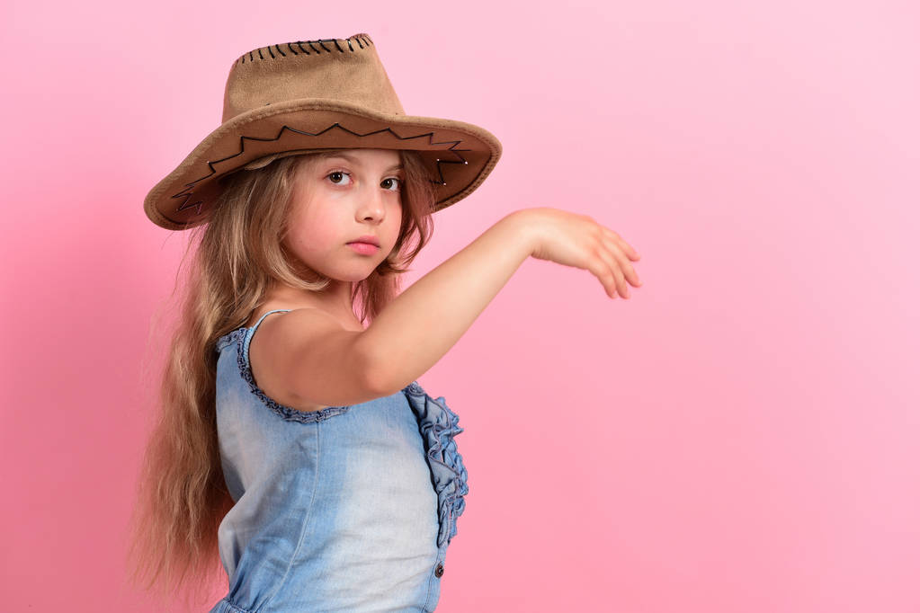 Criança com rosto sério e cabelos longos usa vestido de jeans
 - Foto, Imagem