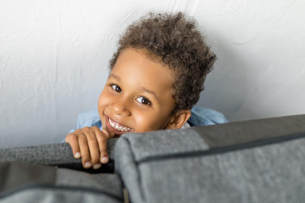 adorable afro chico escondido por sofá
 - Foto, imagen