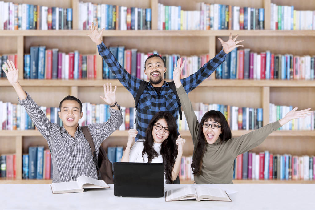 Des étudiants heureux lèvent la main dans la bibliothèque
 - Photo, image