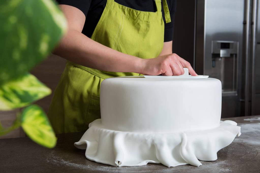 Неузнаваемая женщина в пекарне украшает свадебный торт белой помадкой
 - Фото, изображение