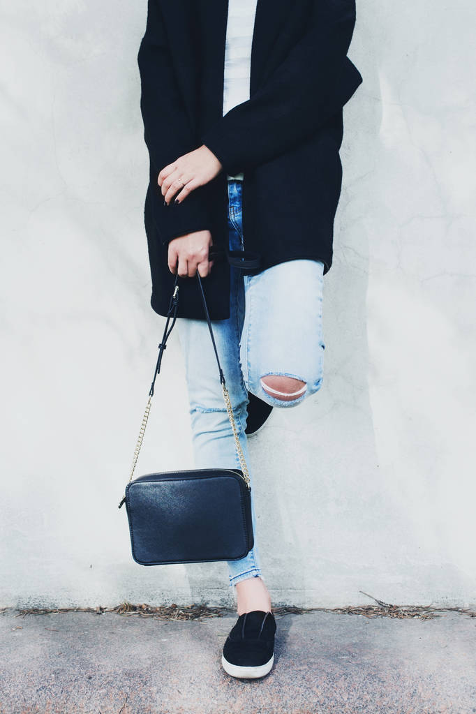 Жінка в чорному пальто, блакитні джинси і сумка біля стіни
 - Фото, зображення