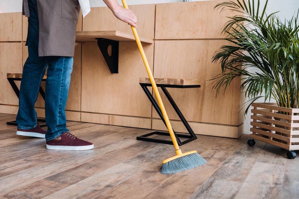 työntekijä puhdistaa lattian luudalla
 - Valokuva, kuva