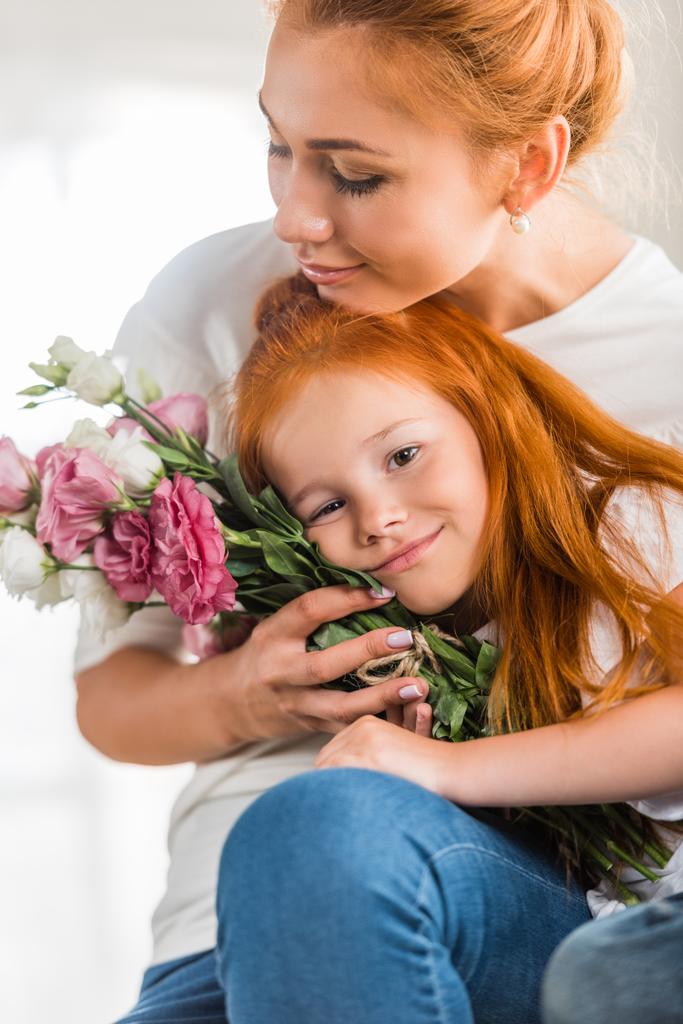 μητέρα με λουλούδια που αγκαλιάζει την μικρή της κόρη - Φωτογραφία, εικόνα