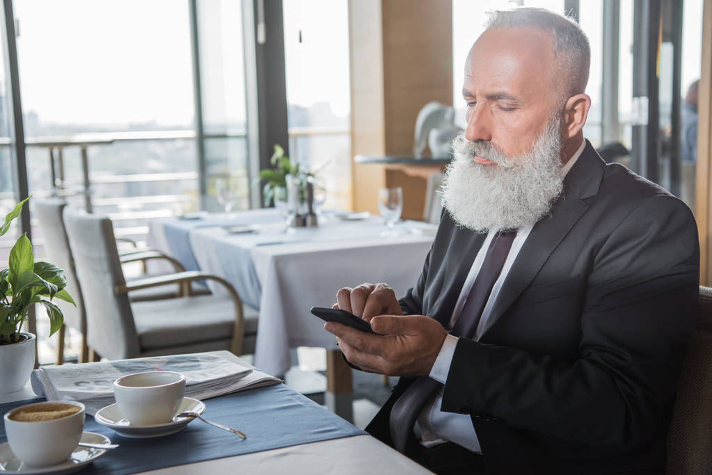 Liikemies käyttää älypuhelinta ravintolassa
 - Valokuva, kuva