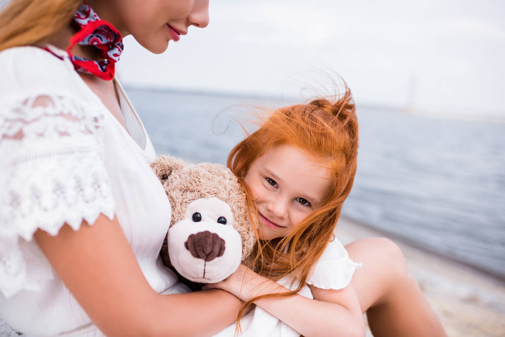 mother and daughter with teddy bear at seashore - Photo, Image