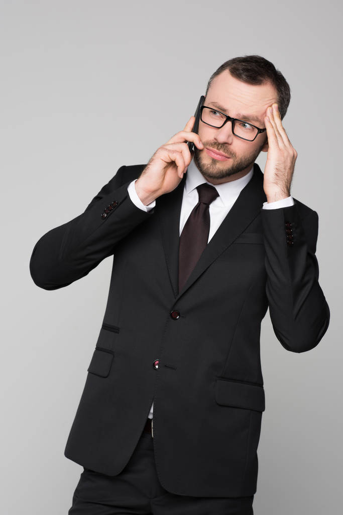 junger Geschäftsmann am Telefon, der seine Schläfe berührt - Foto, Bild
