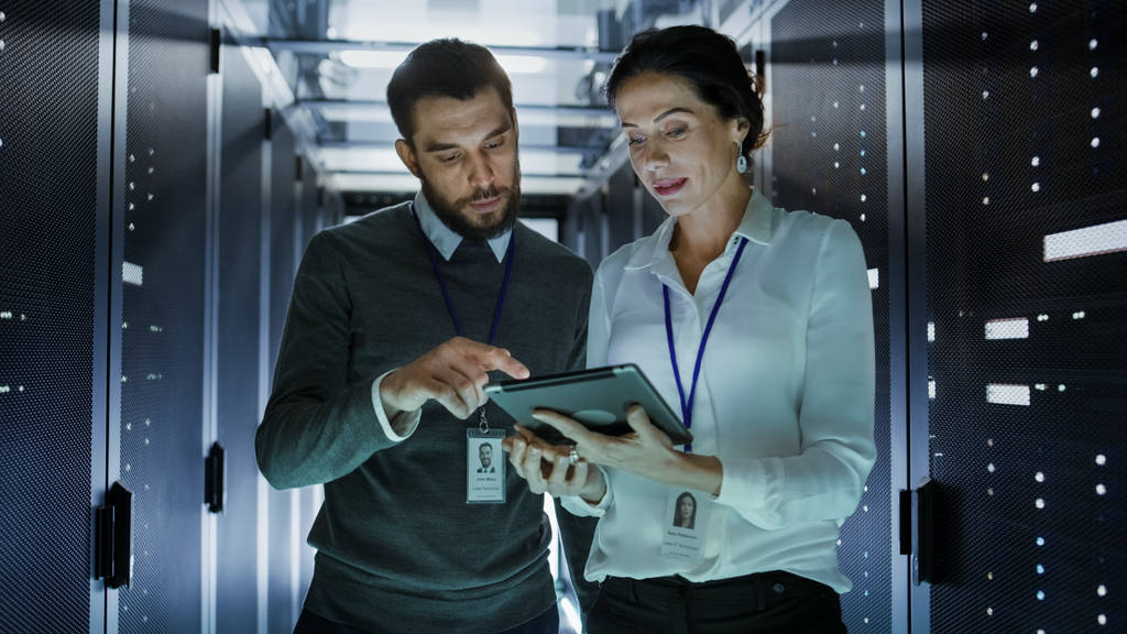 Два IT-инженера прогуливаются в дата-центре / серверной комнате, разговаривая
,  - Фото, изображение