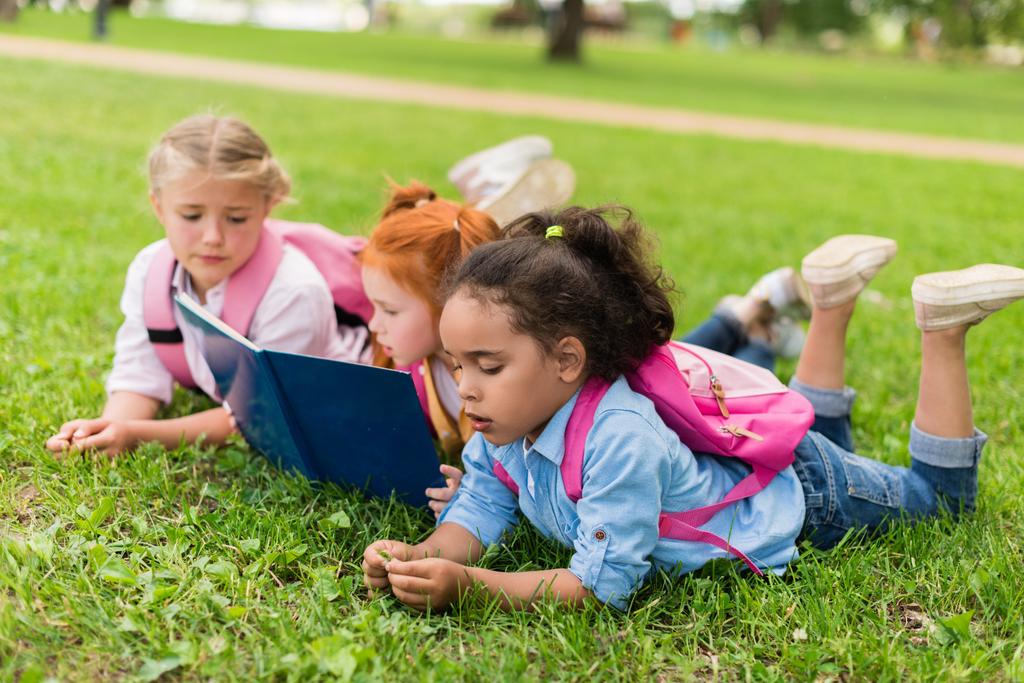 багатоетнічні діти читають книгу на траві
 - Фото, зображення
