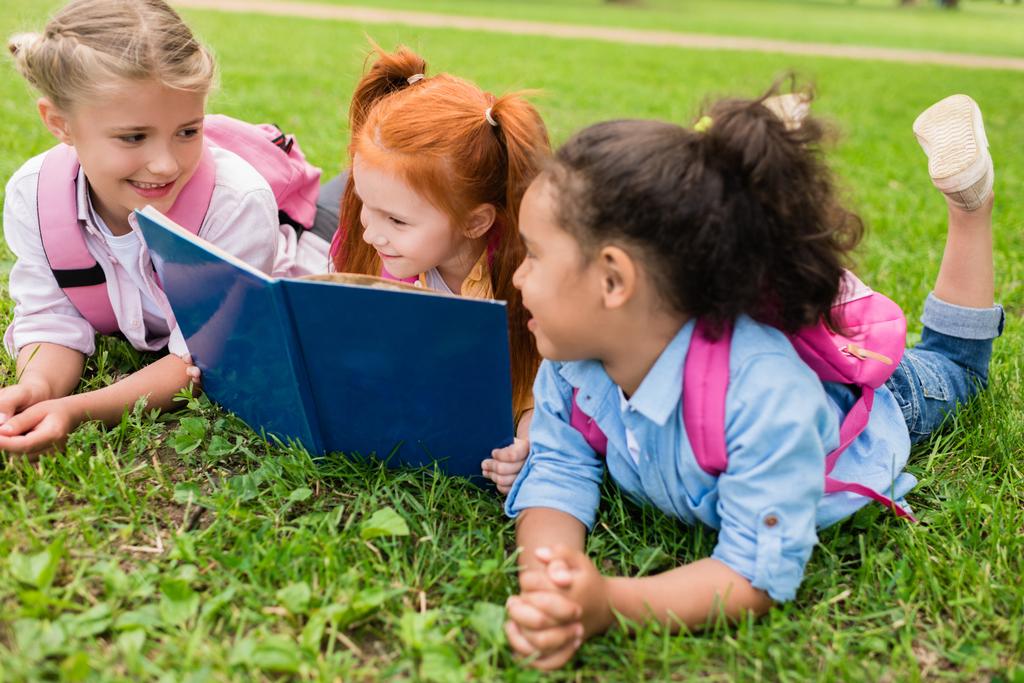 çok ırklı çocuklar çimenlerin üzerinde kitap okuma - Fotoğraf, Görsel