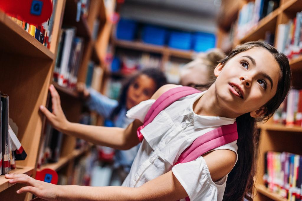 Schoolmeisjes op zoek naar boeken in bibliotheek - Foto, afbeelding