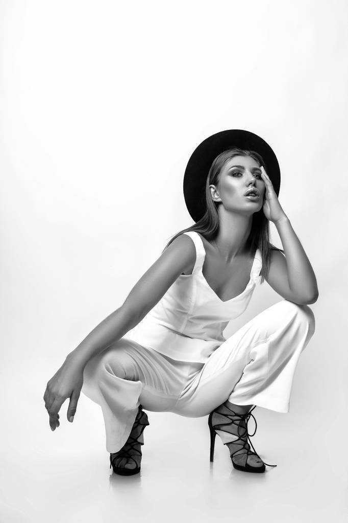 Tyttö valkoisissa vaatteissa ja musta hattu poseeraa studiossa valkoisella taustalla. Musta ja valkoinen phot
 - Valokuva, kuva