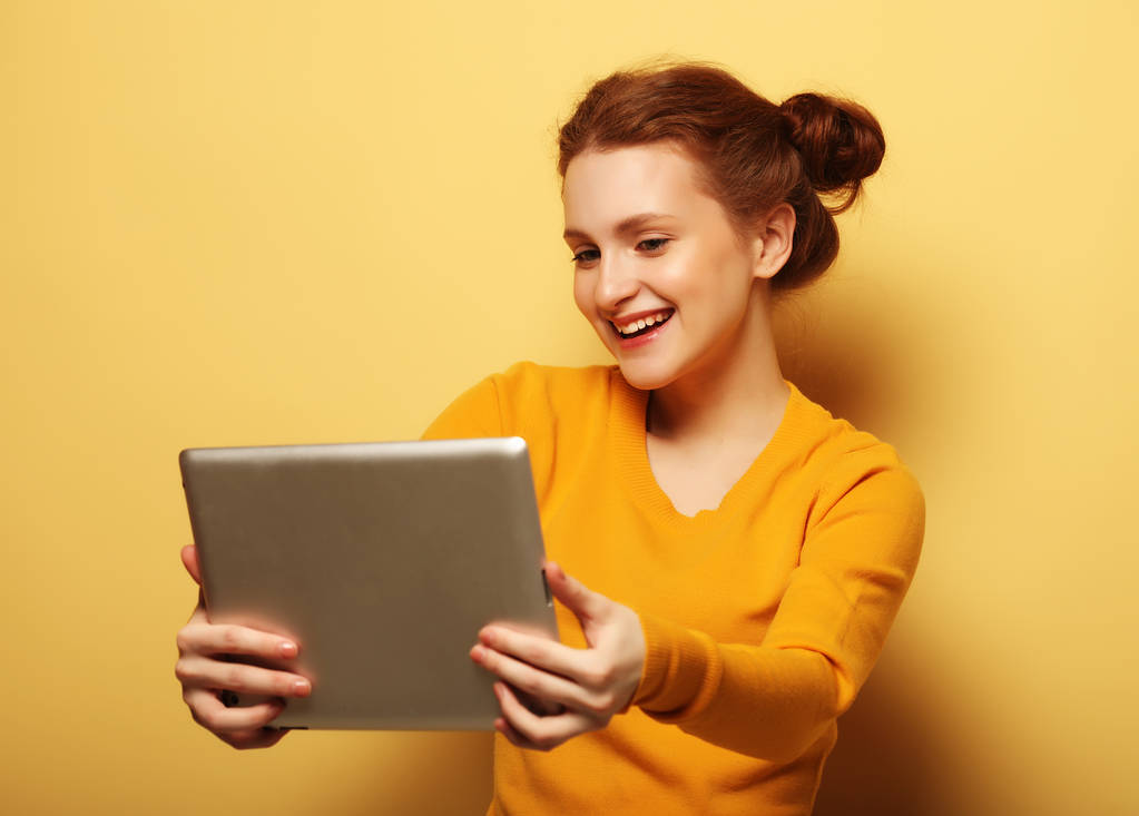 Sarı arka planda tablet bilgisayarı olan genç bir kadın. - Fotoğraf, Görsel