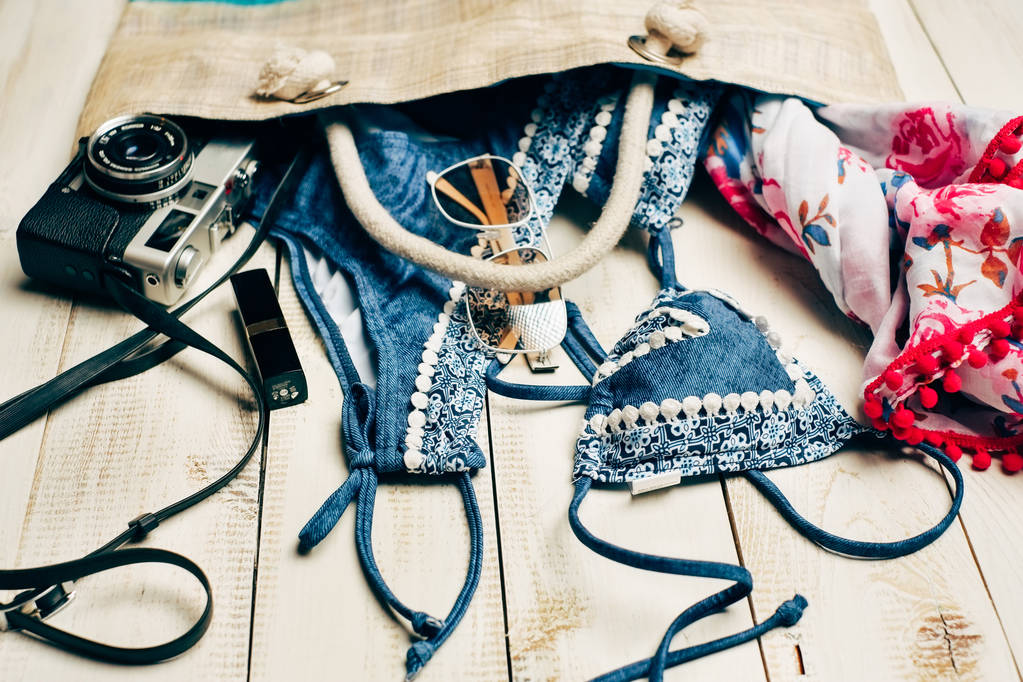  Плоска літня мода з блакитним купальником бікіні всередині сумки та іншими аксесуарами для дівчат на білому дерев'яному фоні
 - Фото, зображення