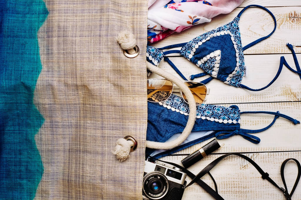  Pose plate de la mode d'été avec maillot de bain bikini bleu à l'intérieur du sac, et d'autres accessoires fille sur fond blanc en bois
 - Photo, image