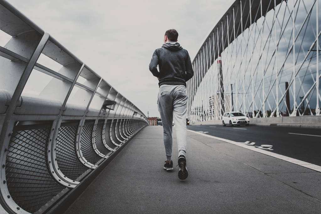 Молодой человек бежит по современному мосту в городе
 - Фото, изображение