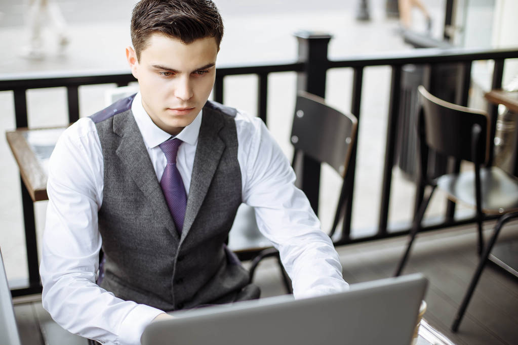 Όμορφος επιχειρηματίας φορώντας κοστούμι και τη χρήση σύγχρονου φορητού υπολογιστή σε εξωτερικούς χώρους, επιτυχημένος manager που εργάζονται στο καφέ κατά τη διάρκεια διάλειμμα και αναζήτηση πληροφοριών στο internet στο φορητό υπολογιστή του - Φωτογραφία, εικόνα