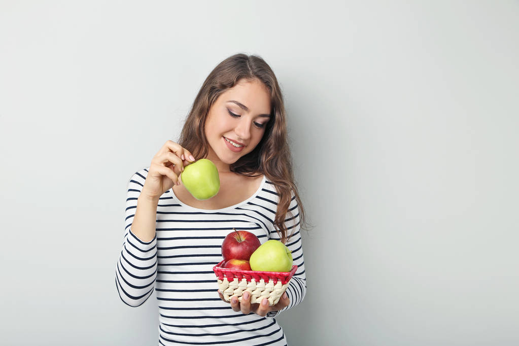 Portrait of young woman with apples on grey background - Photo, Image