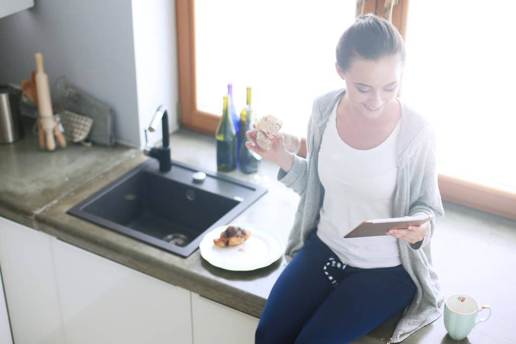Красива молода жінка використовує цифровий планшет на кухні
. - Фото, зображення