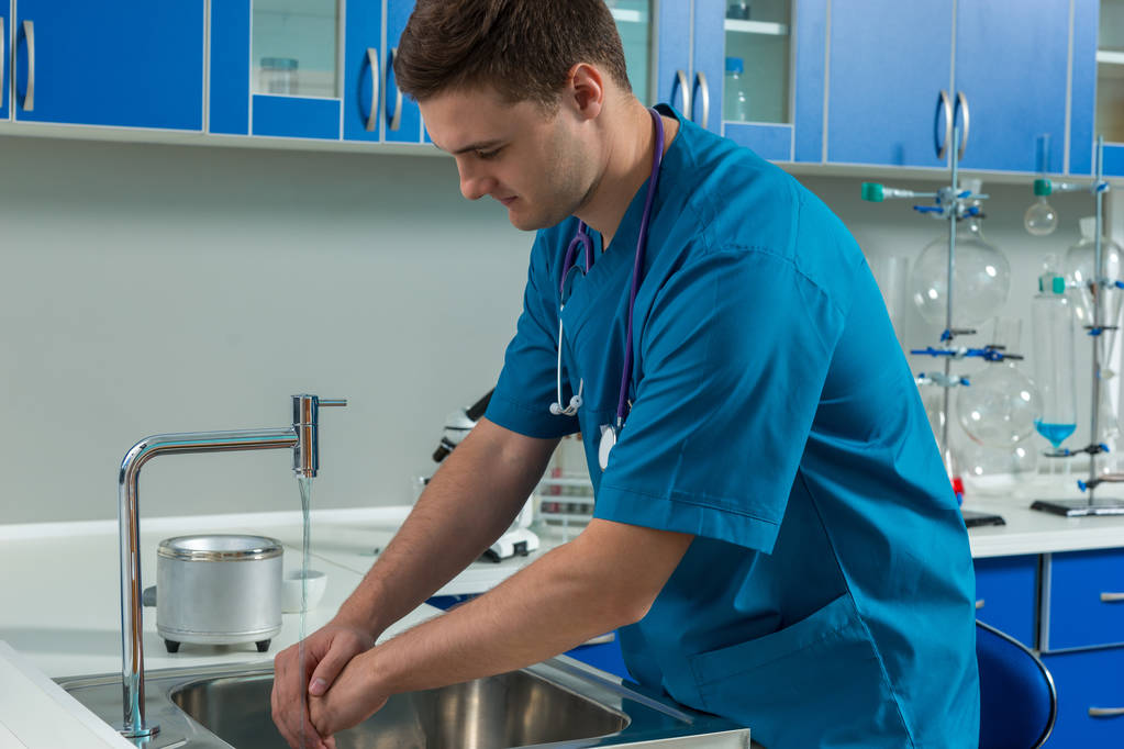 Joven médico de uniforme lavándose las manos en el moderno laboratorio
 - Foto, Imagen