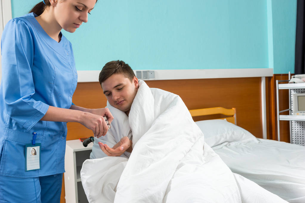 Houkutteleva sairaanhoitaja antaa pillereitä sairaalle potilaalle istuu Wheelcha
 - Valokuva, kuva