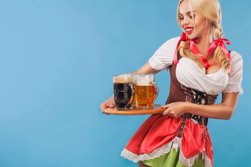Menina Oktoberfest sexy nova - garçonete, vestindo um vestido tradicional da Baviera, servindo canecas de cerveja grandes no fundo azul
. - Foto, Imagem
