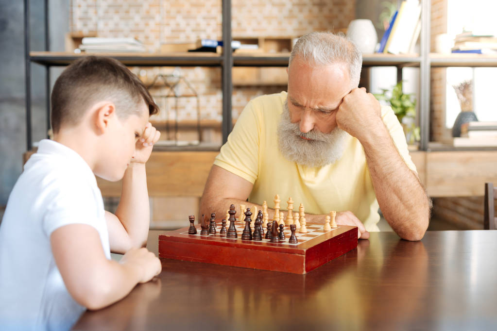 Концентрированный дедушка играет в шахматы со своим внуком
 - Фото, изображение