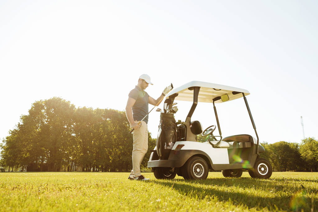 Golfeur prenant des clubs d'un sac dans une voiturette de golf
 - Photo, image