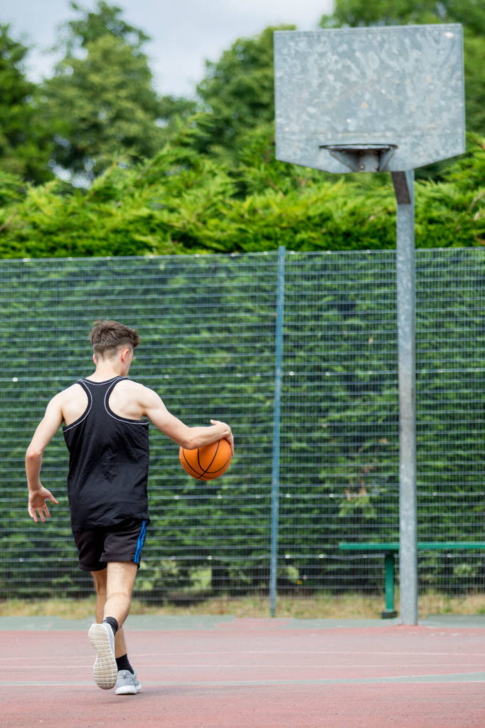 Εφηβικό αγόρι γερός μια μπάλα του μπάσκετ στο γήπεδο - Φωτογραφία, εικόνα